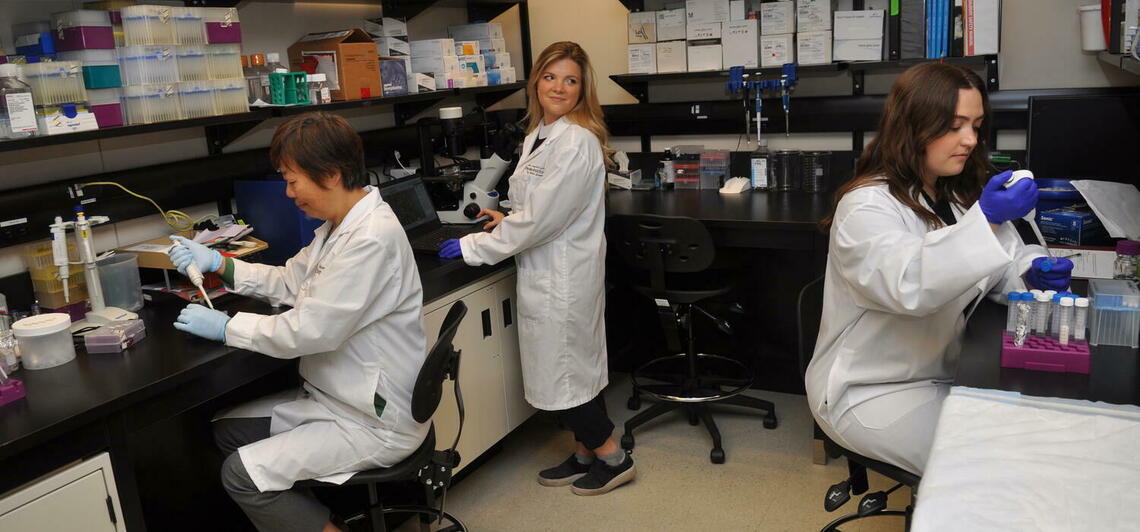 three women in lab coats work in a research lab