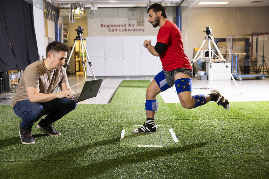 man with a laptop studies another man wearing motion-capture sensors