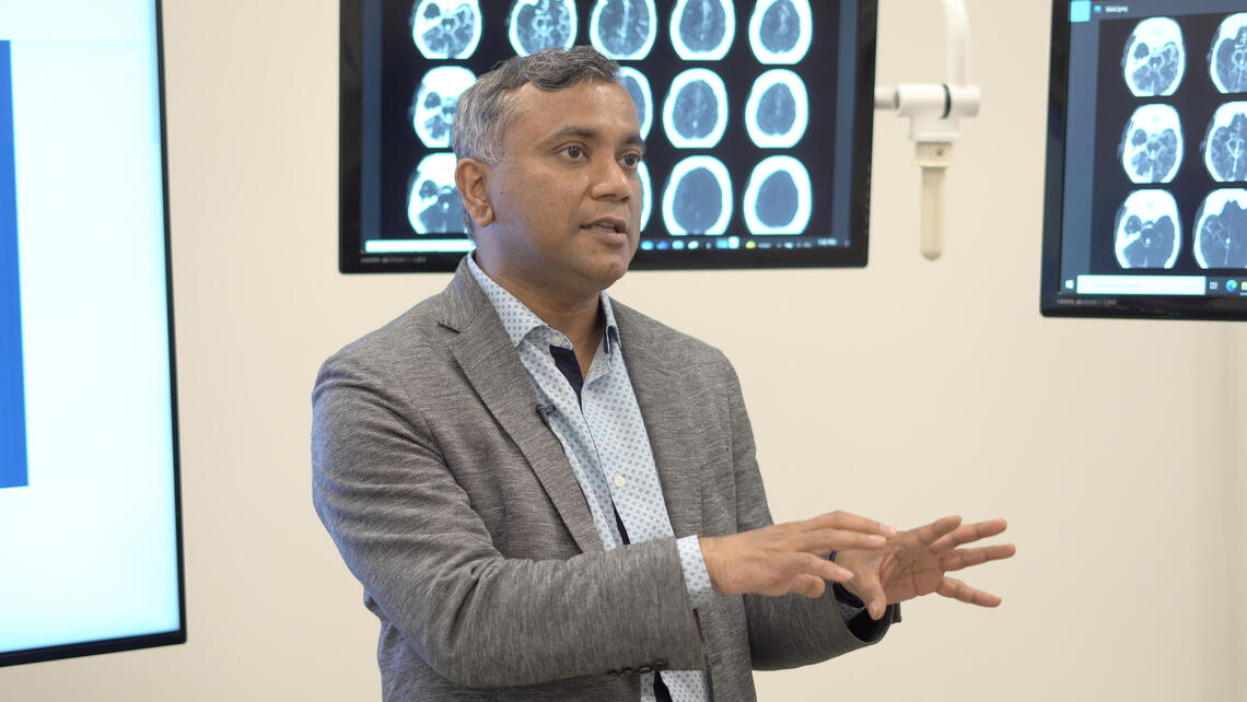 Bijoy Menon stands in front of a number of brain scans.  