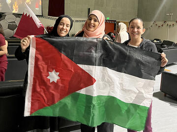 Three people hold up a flag to the camera and smile