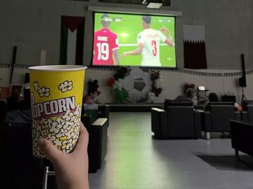 A person holds popcorn up while watching the soccer game