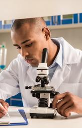 young man in a lab next to microscope
