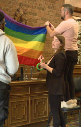 People hanging a pride flag inside a community room.